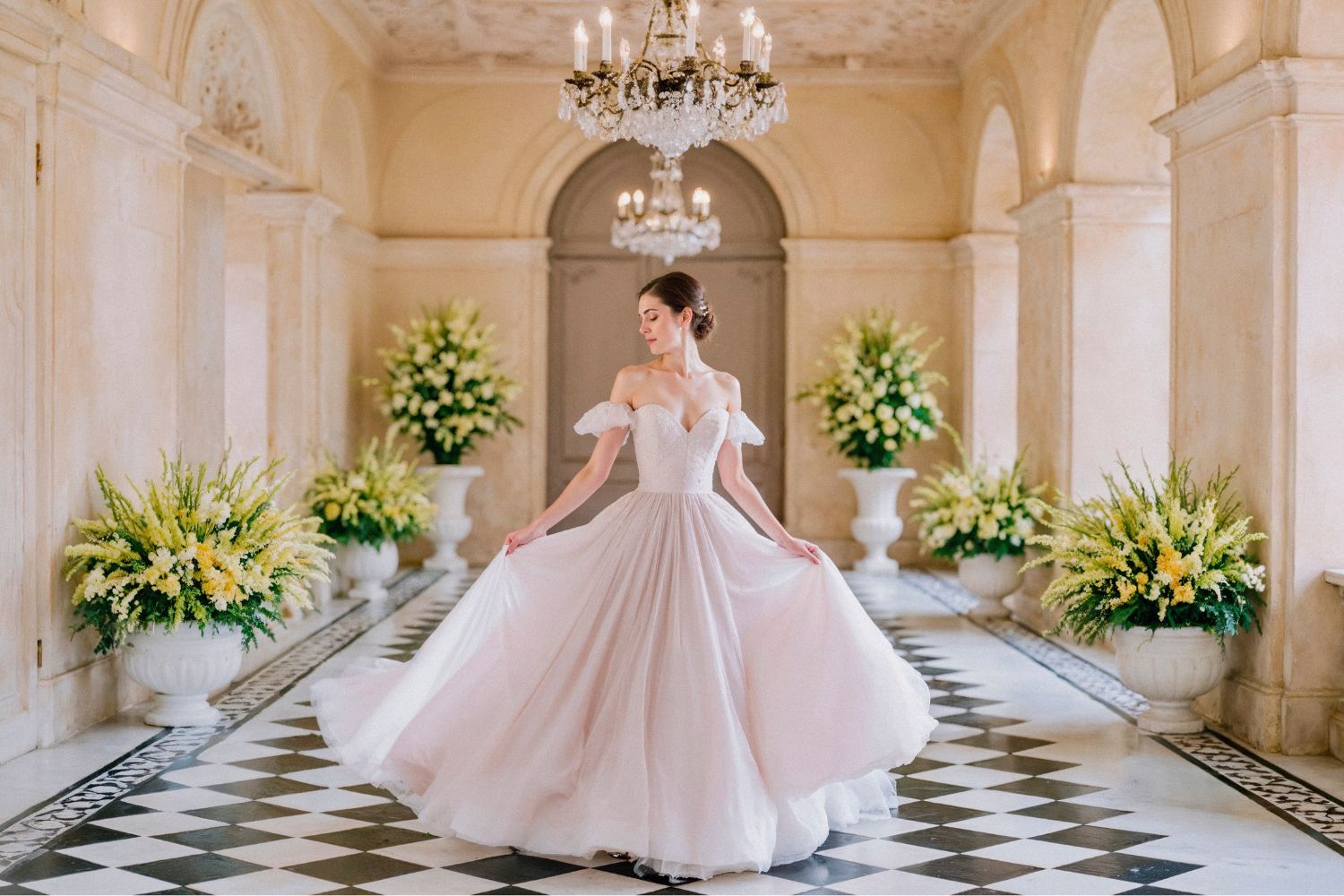 Panna młoda w klasycznej sukni ślubnej pozująca we wnętrzu zamku z kolumnami, żyrandolami i kwiatową dekoracją – wesele w zamku z bajkowym klimatem.